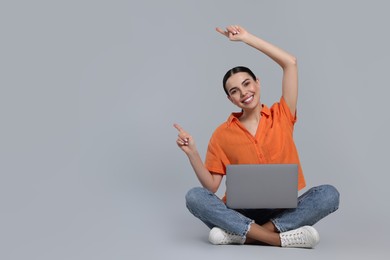 Happy woman with laptop pointing at something on light gray background, space for text