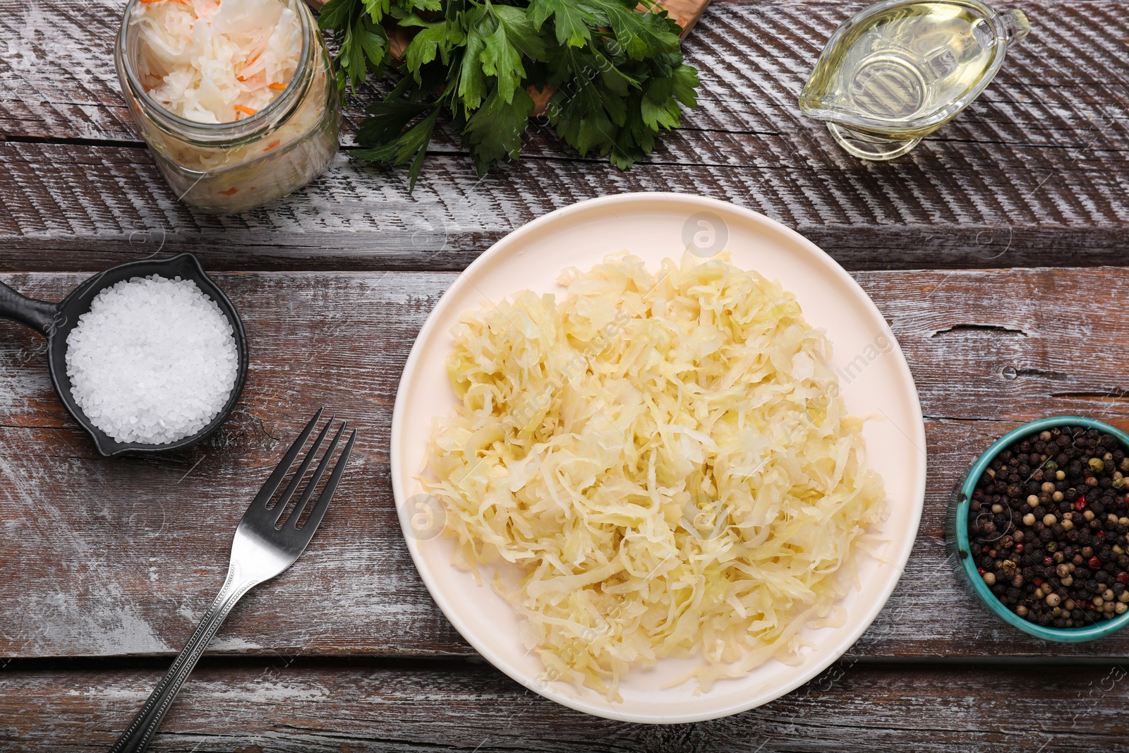 Photo of Plate of tasty sauerkraut and ingredients on wooden table, flat lay