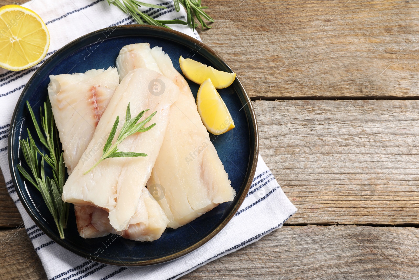 Photo of Pieces of raw cod fish, rosemary and lemon on wooden table, top view. Space for text