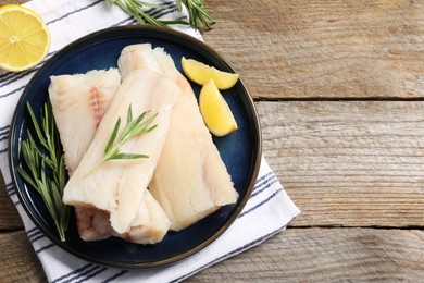 Photo of Pieces of raw cod fish, rosemary and lemon on wooden table, top view. Space for text