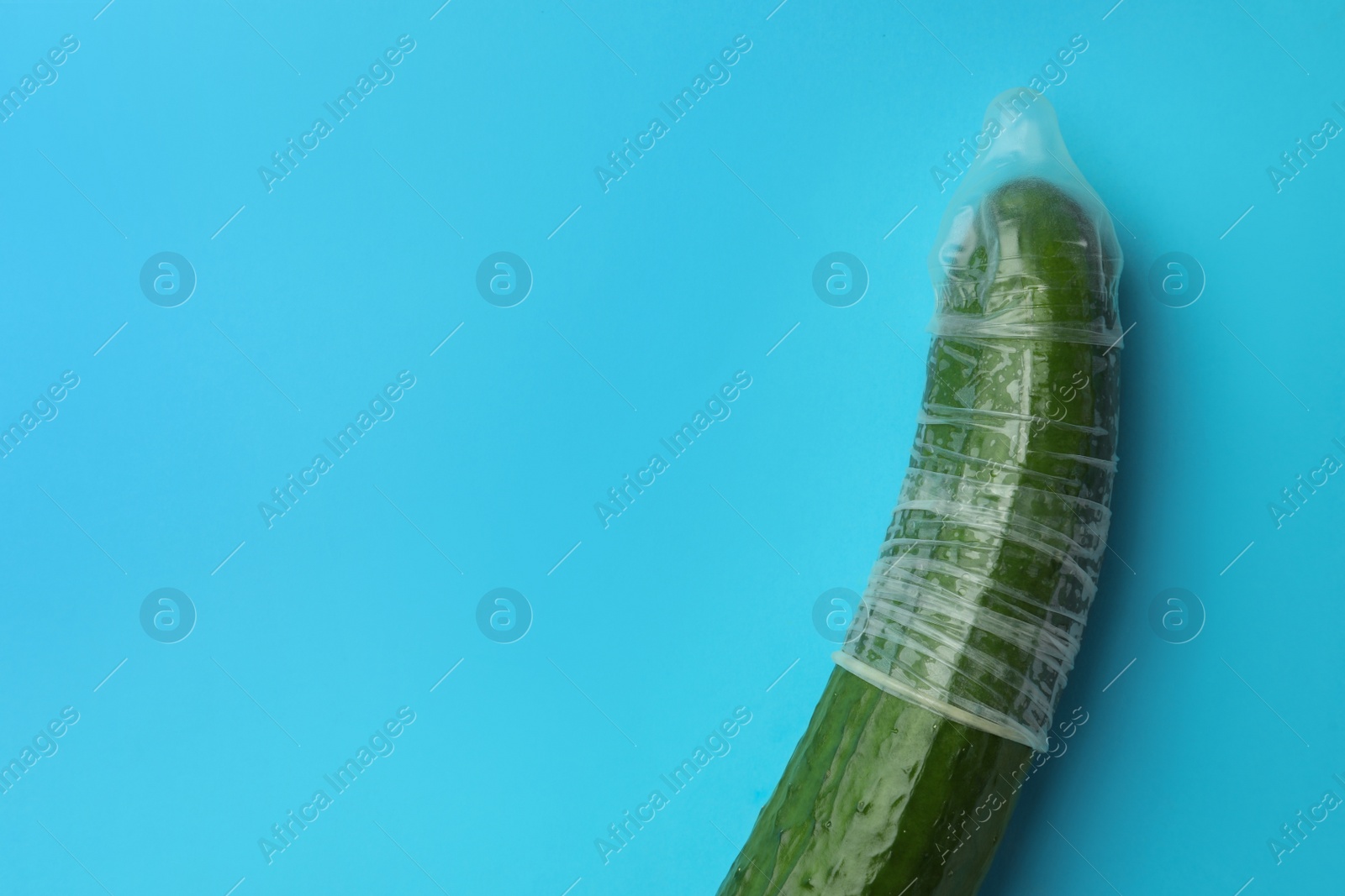 Photo of Cucumber with condom on light blue background, top view and space for text. Safe sex concept