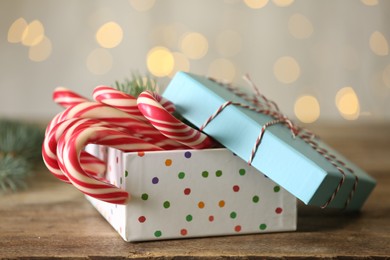 Photo of Christmas candy canes in gift box on wooden table against blurred lights