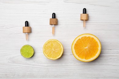 Photo of Pipettes with citrus essential oils and fresh fruits on white wooden table, flat lay