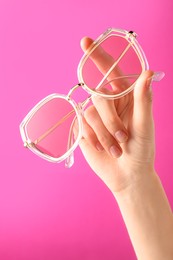 Woman holding stylish sunglasses on pink background, closeup of hand