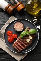 Photo of Delicious grilled beef steak served with spices and tomatoes on black wooden table, flat lay