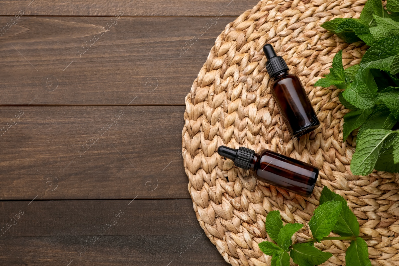 Photo of Bottles of essential oil and mint on wooden table, top view. Space for text