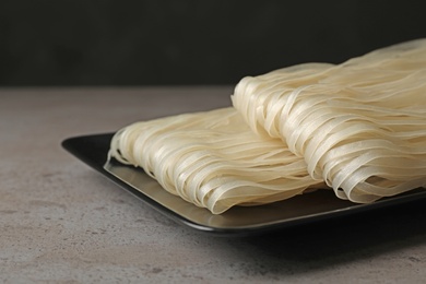 Plate with raw rice noodles on grey table, closeup. Delicious pasta