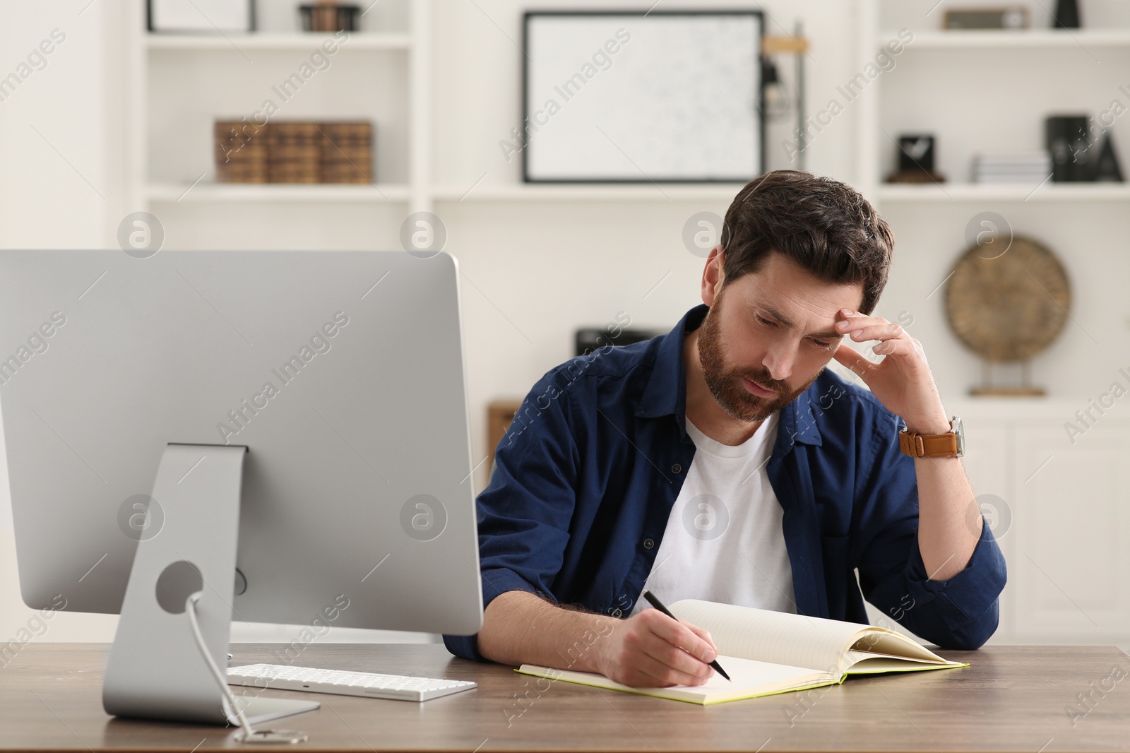 Photo of Home workplace. Man taking notes near computer at wooden desk in room