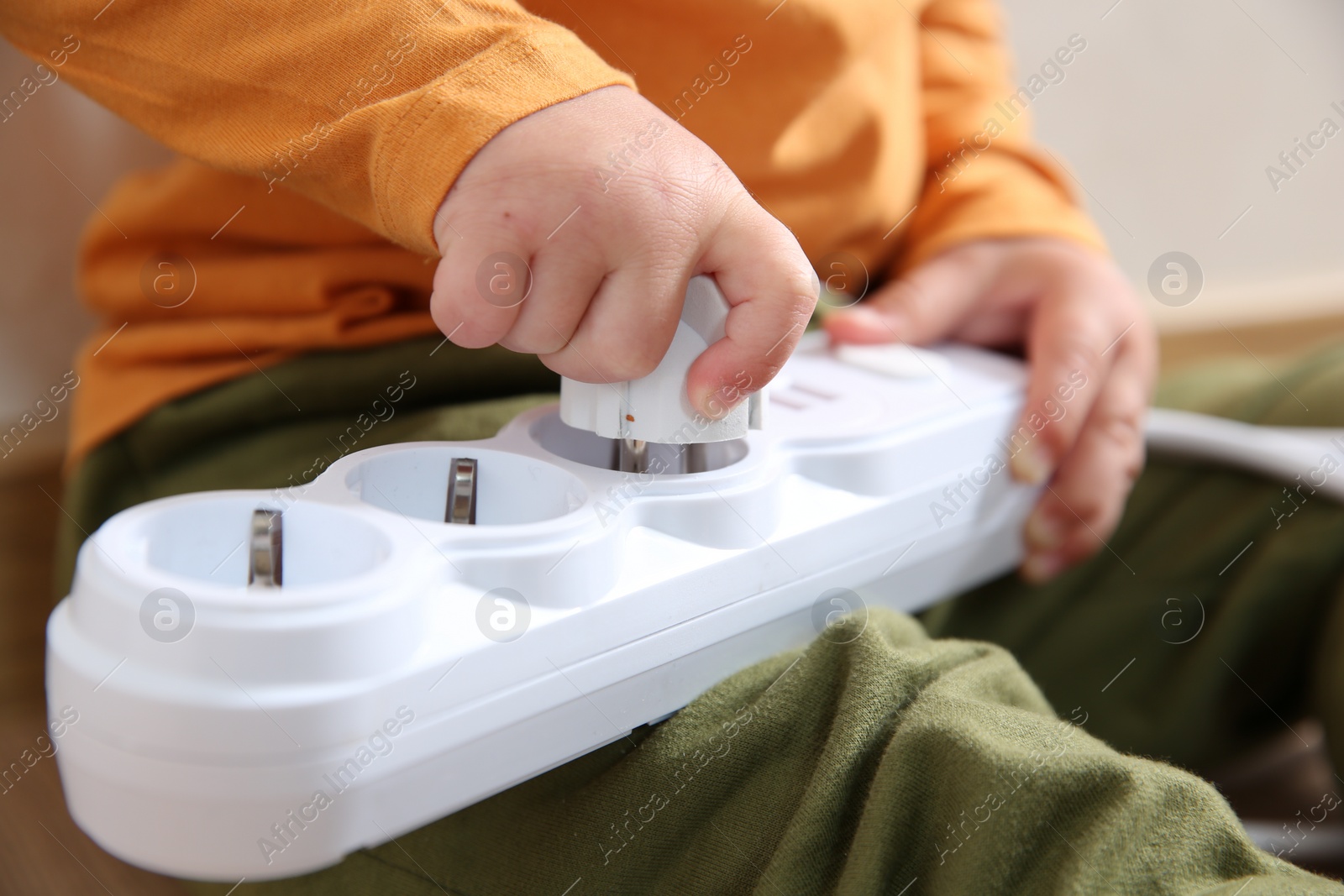 Photo of Little child playing with power strip and plug indoors, closeup