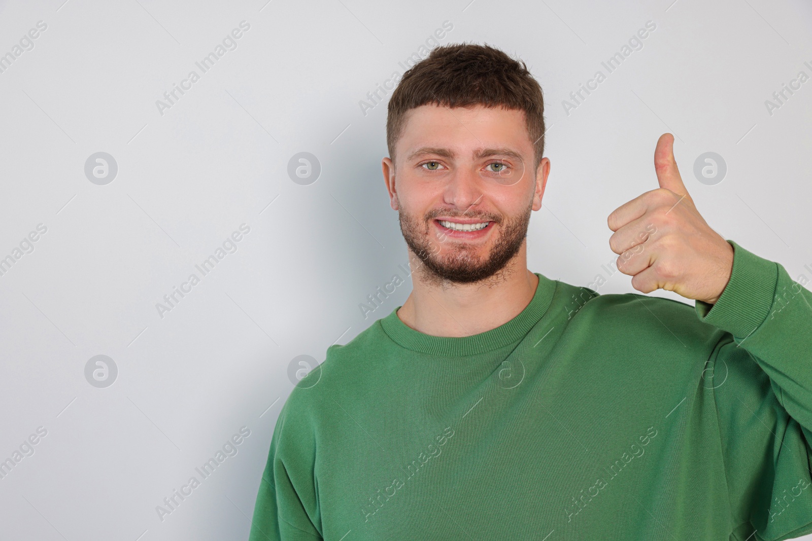 Photo of Young man showing thumb up on white background, space for text