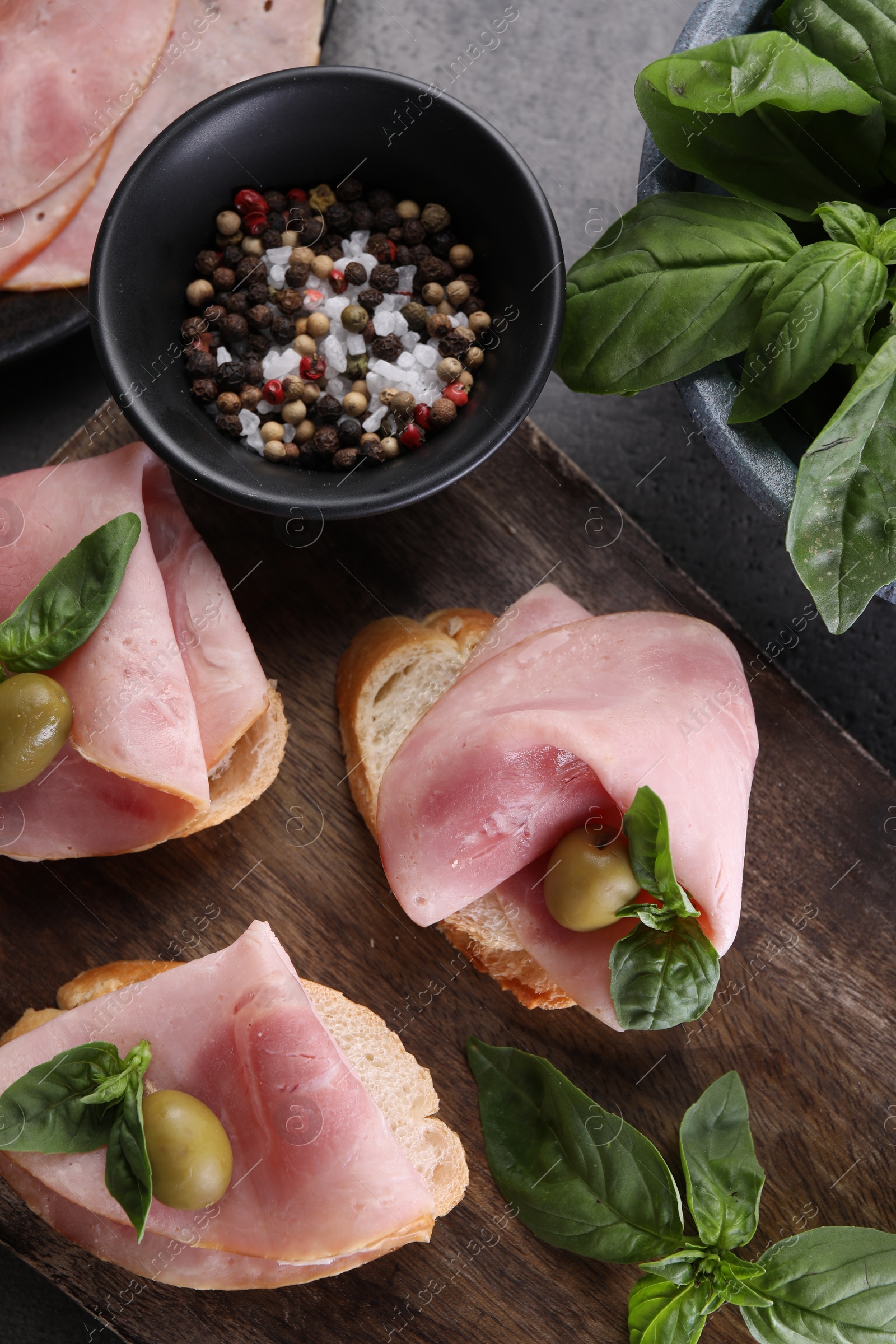 Photo of Delicious sandwiches with ham, basil, olives and spices on grey table, flat lay