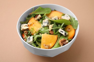 Photo of Tasty salad with persimmon, blue cheese and walnuts served on light brown background