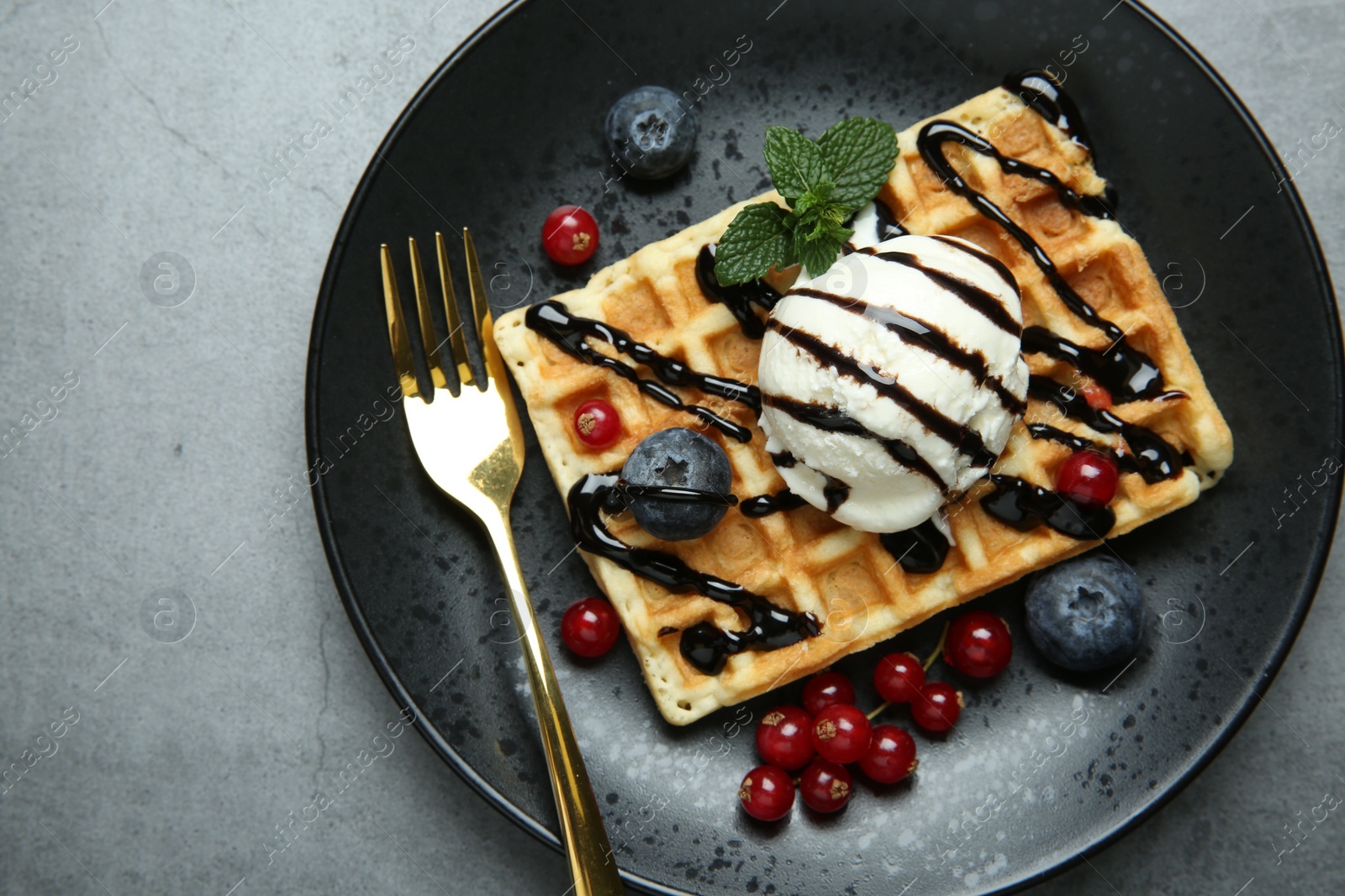 Photo of Delicious Belgian waffle with ice cream, berries and chocolate sauce on grey textured table, top view