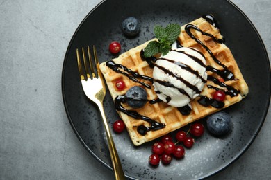 Photo of Delicious Belgian waffle with ice cream, berries and chocolate sauce on grey textured table, top view