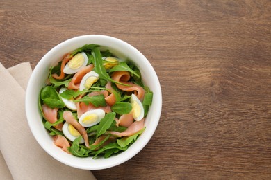 Photo of Delicious salad with boiled eggs, salmon and arugula on wooden table, top view. Space for text