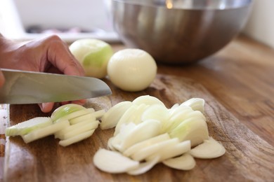 Photo of Woman cutting fresh ripe onion on wooden board, closeup