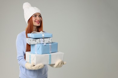 Photo of Young woman in hat and sweater with Christmas gifts on light grey background, space for text