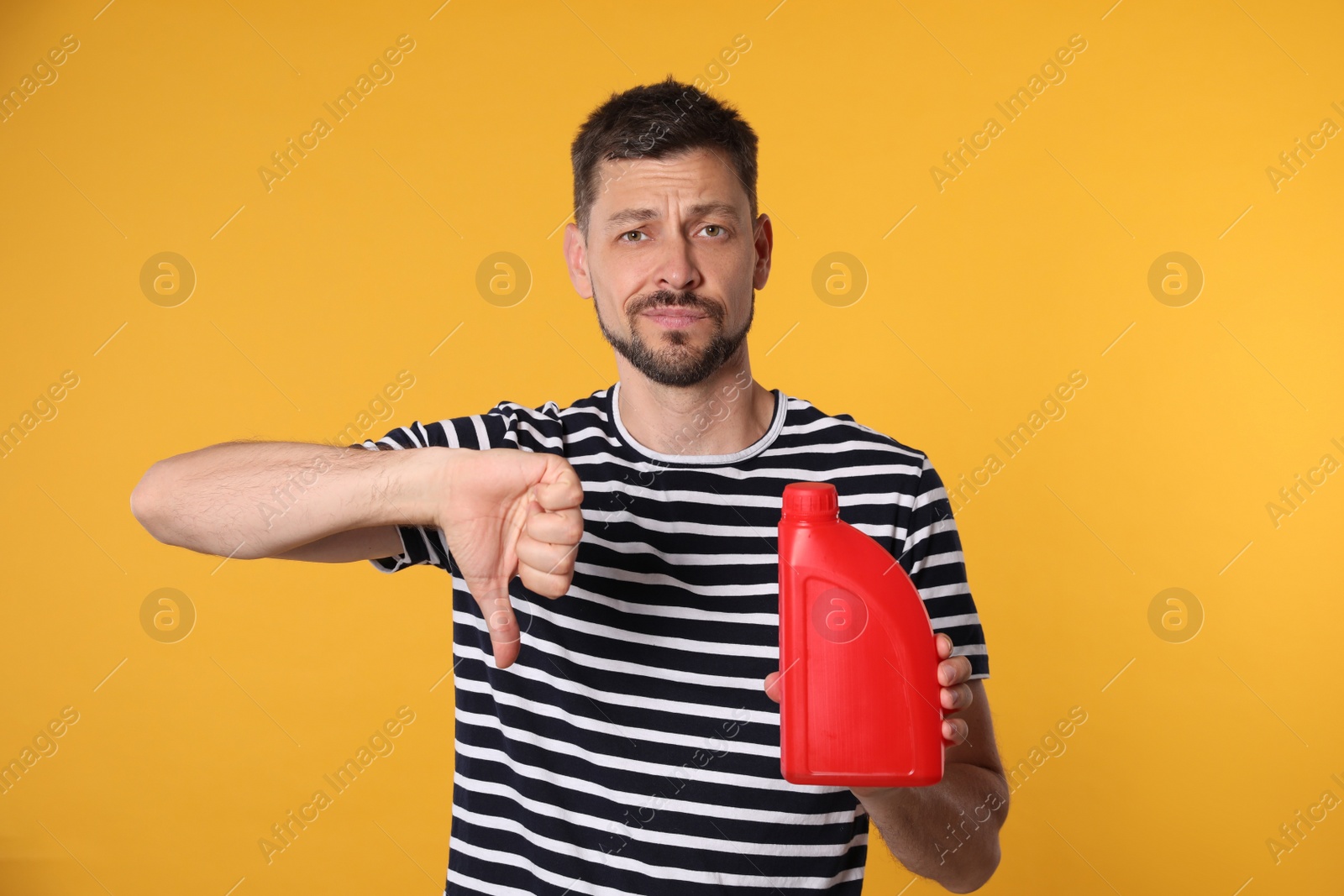 Photo of Man holding red container of motor oil and showing thumbs down on orange background