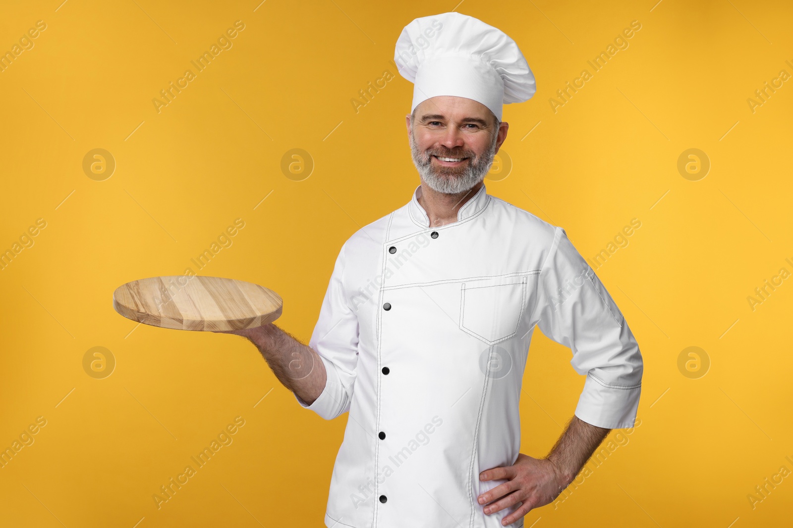 Photo of Happy chef in uniform with wooden board on orange background