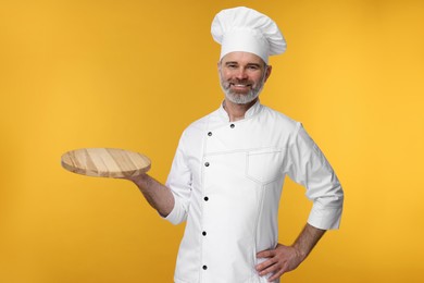 Happy chef in uniform with wooden board on orange background