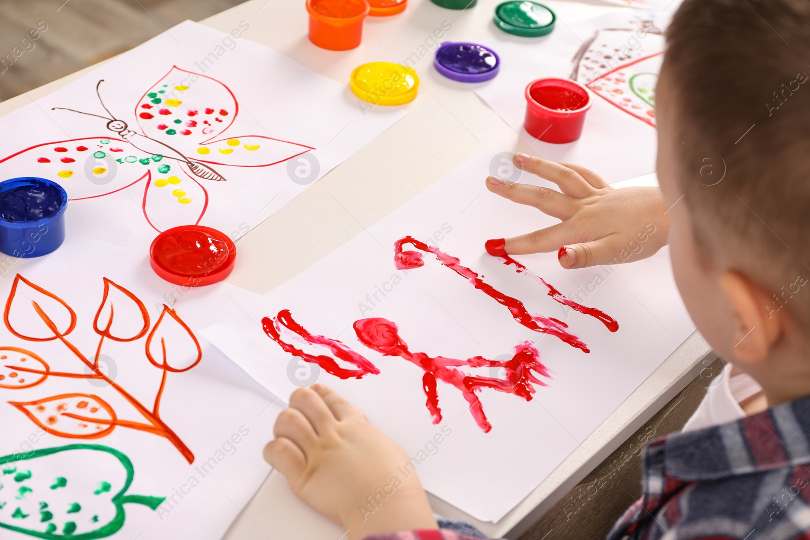 Photo of Little boy painting with finger at white table indoors, closeup