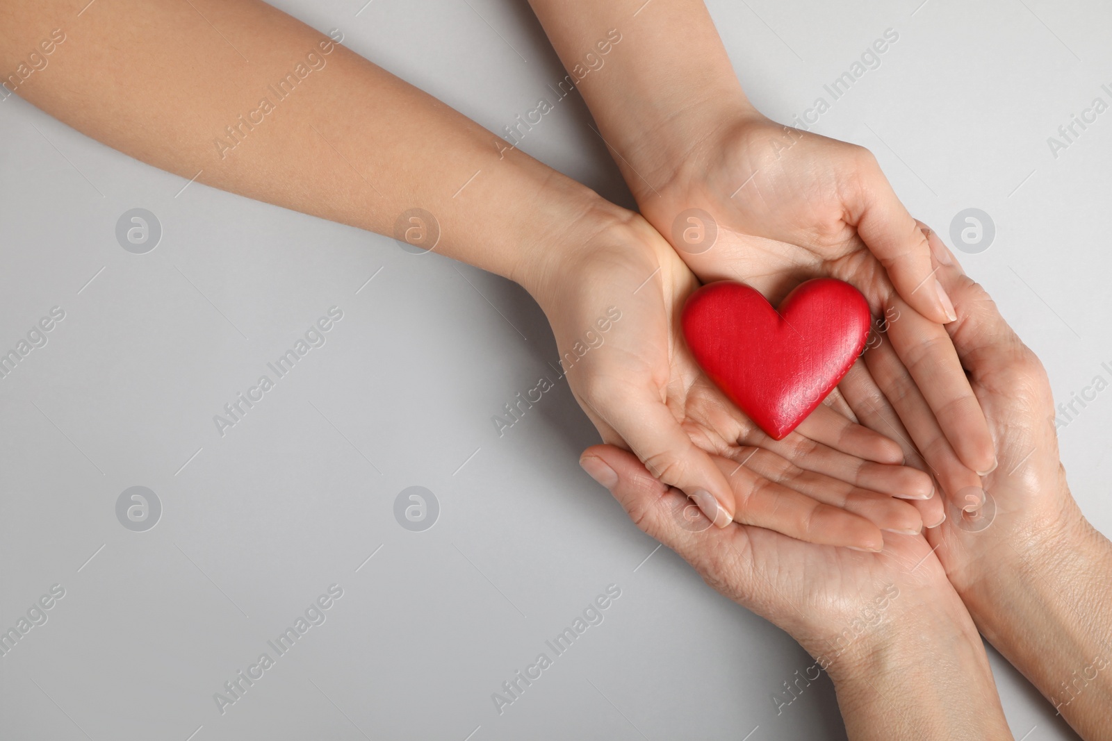 Photo of Young and elderly women holding red heart on light grey background, closeup. Space for text