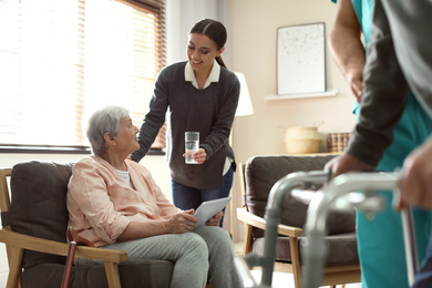 Photo of Care worker giving water to elderly woman with tablet in geriatric hospice