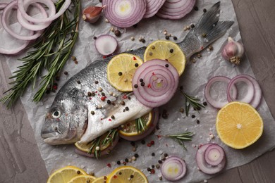 Photo of Raw dorado fish with spices, lemon and onion on grey textured table, top view