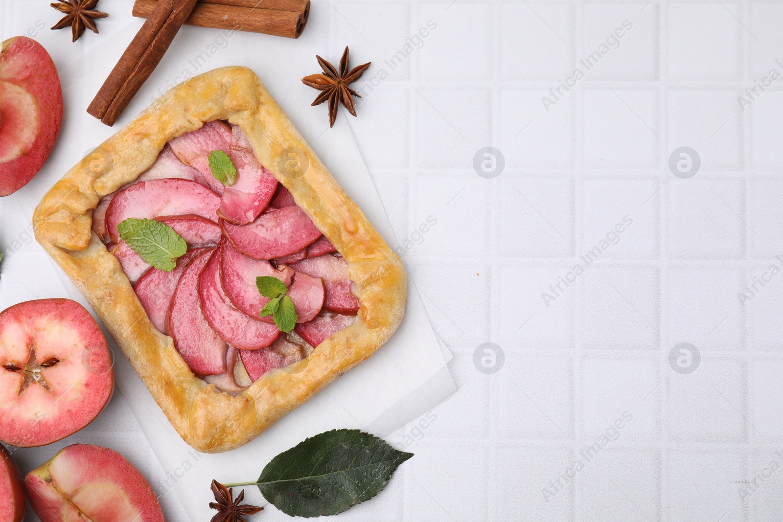 Photo of Delicious apple galette with mint and ingredients on white tiled table, flat lay. Space for text