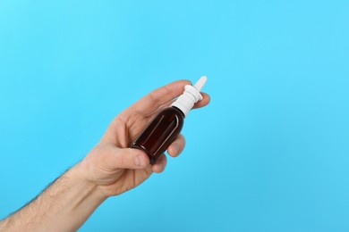 Photo of Man holding nasal spray on light blue background, closeup. Space for text