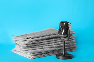 Photo of Newspapers and vintage microphone on light blue background. Journalist's work