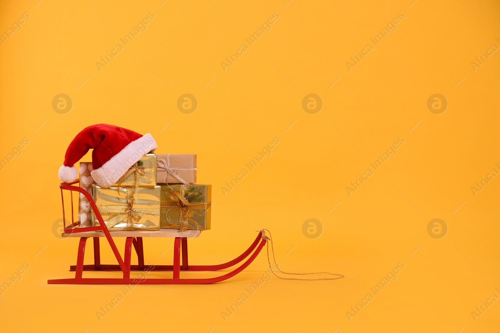 Photo of Sleigh with gift boxes and Santa hat on yellow background. Space for text