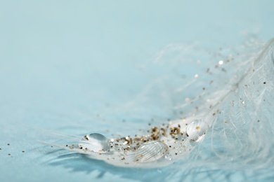 Closeup view of beautiful feather with dew drops and glitter on light blue background, space for text