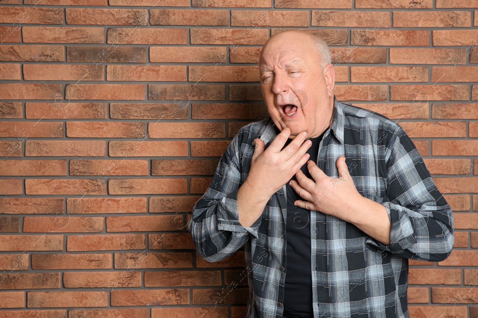 Photo of Senior man suffering from cough near brick wall. Space for text