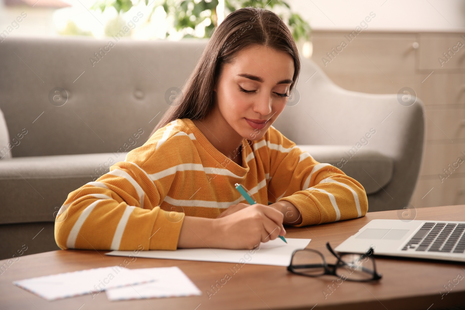 Photo of Woman writing letter at wooden table in room