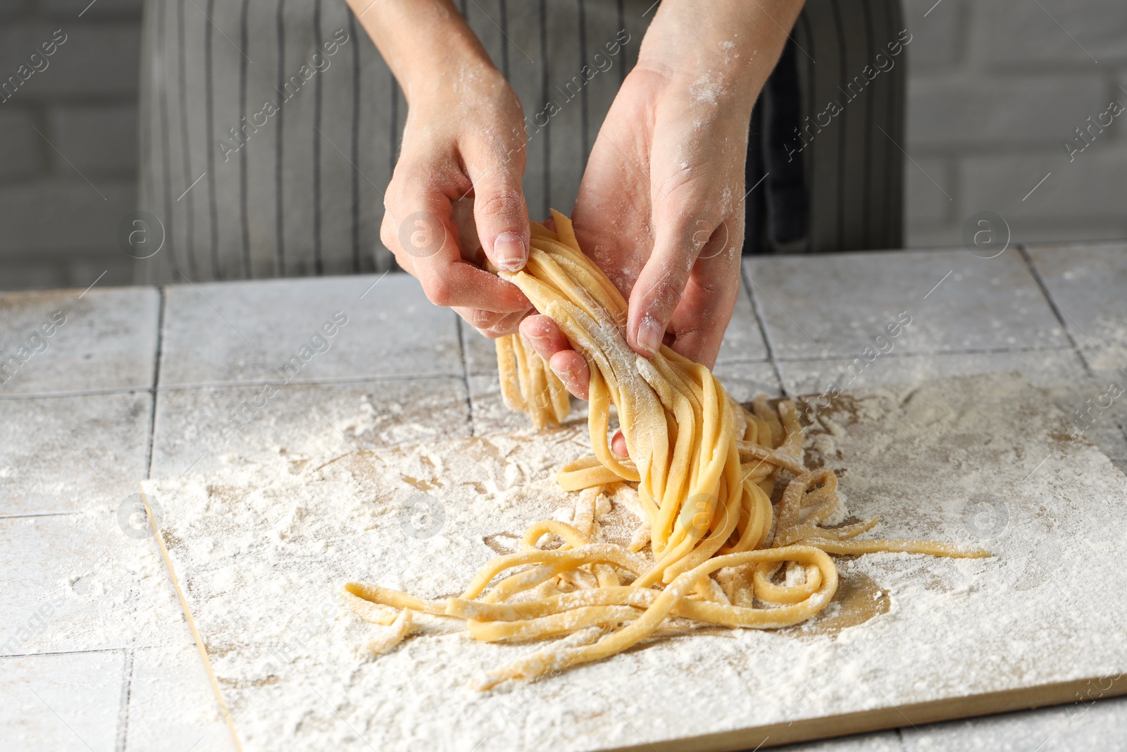 Photo of Woman with homemade pasta at light tiled table, closeup