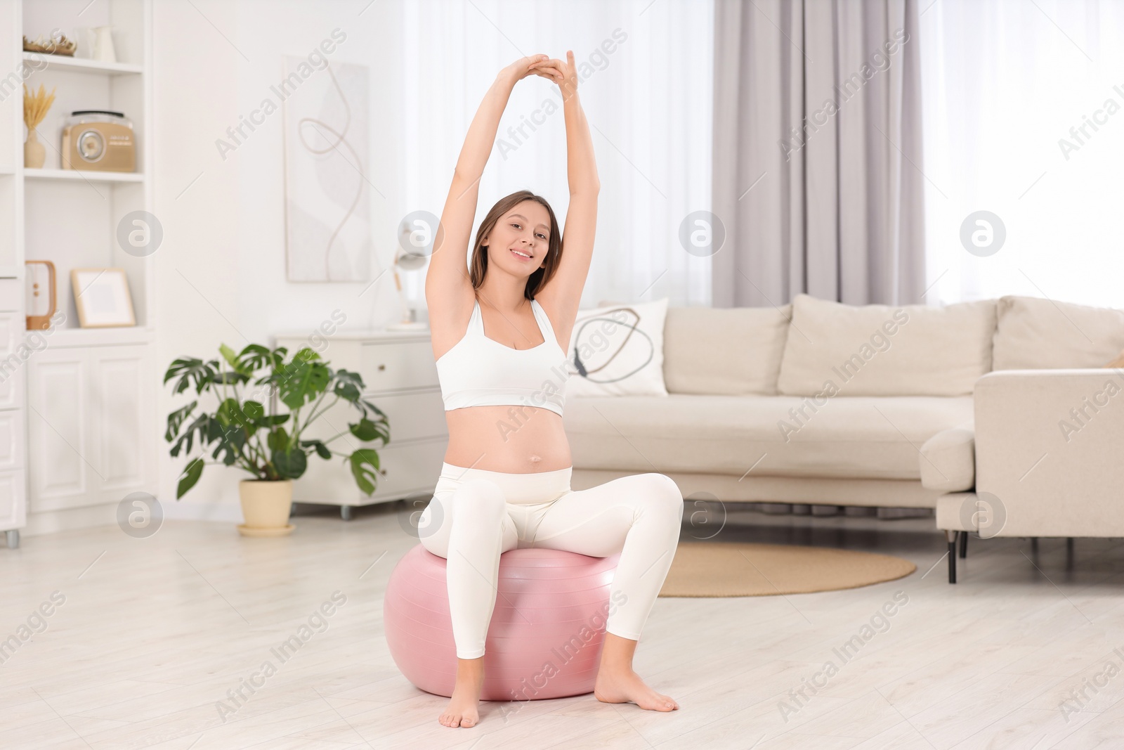 Photo of Pregnant woman doing exercises on fitness ball in room. Home yoga