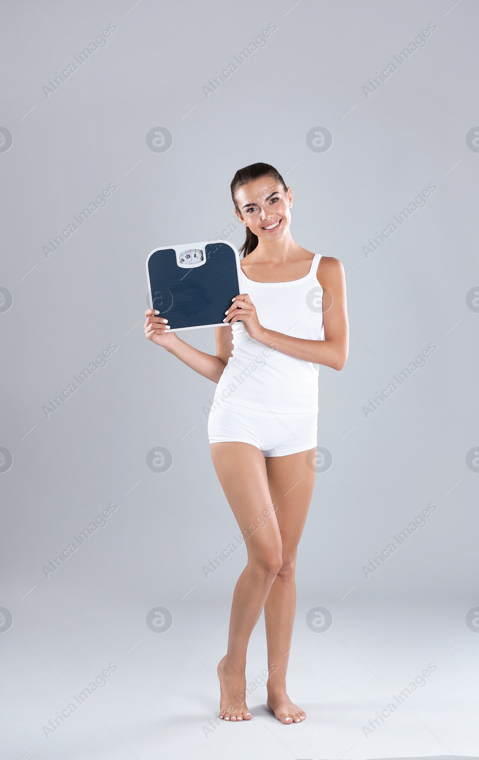 Photo of Happy young woman with scales on color background. Weight loss motivation