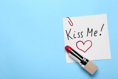 Photo of Card with phrase Kiss Me and drawn heart, lipstick on light blue background, top view. Space for text