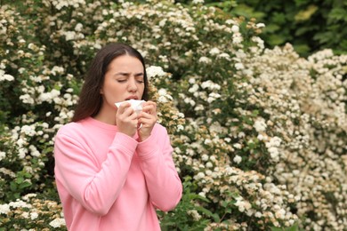 Woman suffering from seasonal pollen allergy near blossoming tree on spring day