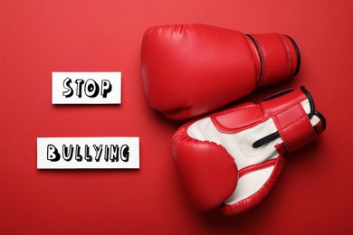 Phrase Stop Bullying and boxing gloves on red background, flat lay