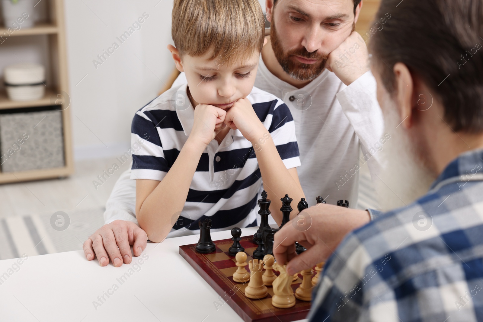 Photo of Family playing chess together at table in room