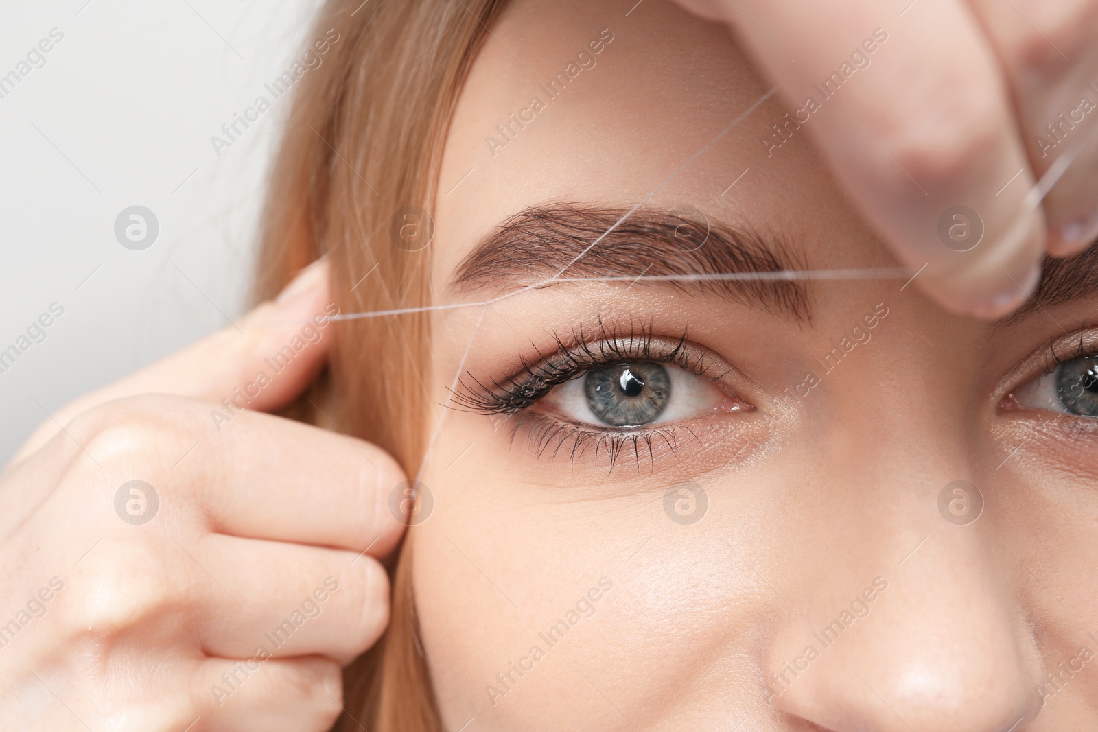 Photo of Young woman having professional eyebrow correction procedure in beauty salon