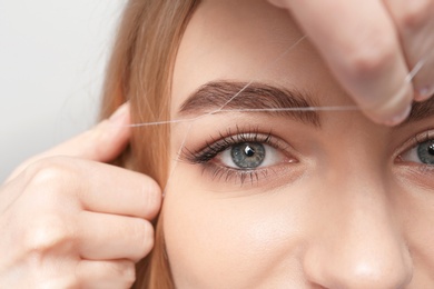 Photo of Young woman having professional eyebrow correction procedure in beauty salon