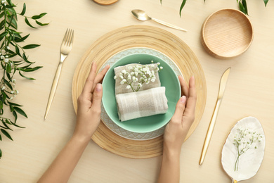 Photo of Woman setting table with flowers for festive dinner, top view