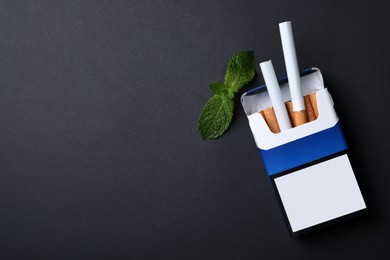 Pack of menthol cigarettes and mint on black background, flat lay. Space for text