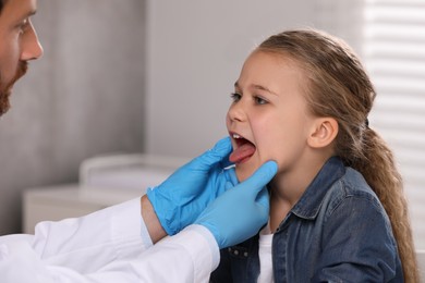 Doctor in medical gloves examining girl`s oral cavity indoors