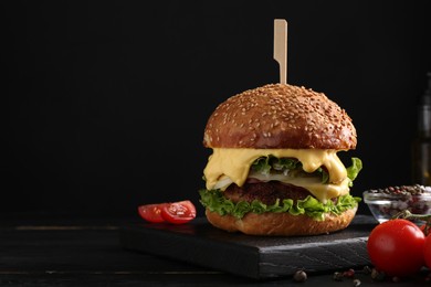 Photo of Tasty vegetarian burger, tomatoes and spices on black wooden table. Space for text