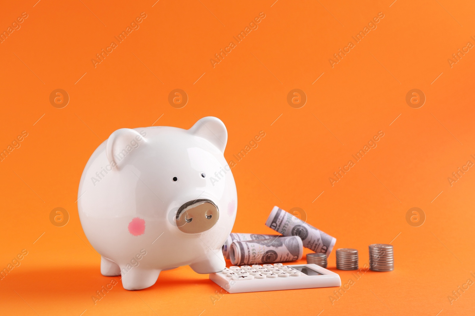 Photo of Financial savings. Piggy bank, dollar banknotes, coins and calculator on orange background