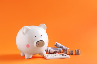 Photo of Financial savings. Piggy bank, dollar banknotes, coins and calculator on orange background